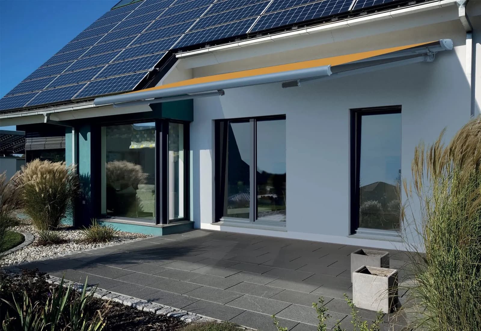 Store banne déployé sur la terrasse d'une maison équipée de panneaux solaires